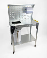 A mobile cleaning station on wheels, featuring a small plastic sink with metal grate on top, a roll of paper towel, and storage shelves underneath.
